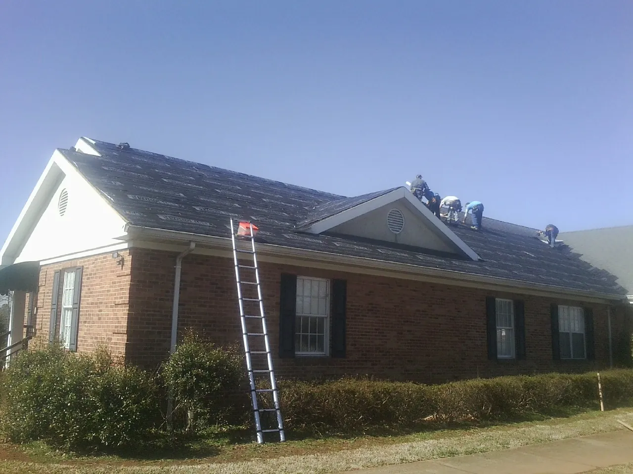 Crew tearing shingles off a brick ranch roof with a ladder set — Metal Roof Repair work by our crew in Ellisville