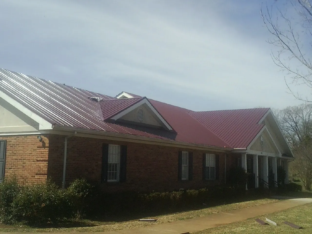 Red metal roof with gabled entries on a long brick building, from a Hail Damage Roof Repair job in Ellisville