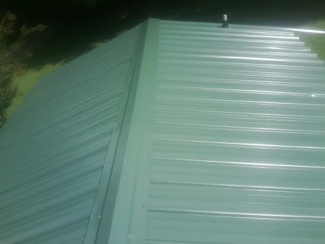 New green metal panels meeting at the ridge of a roof — Flat Roof Repair work by our crew in Ellisville