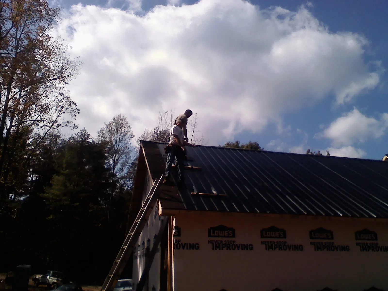 Roofer fastening dark metal panels high against a cloudy sky, from a Roof Inspection job in Ellisville