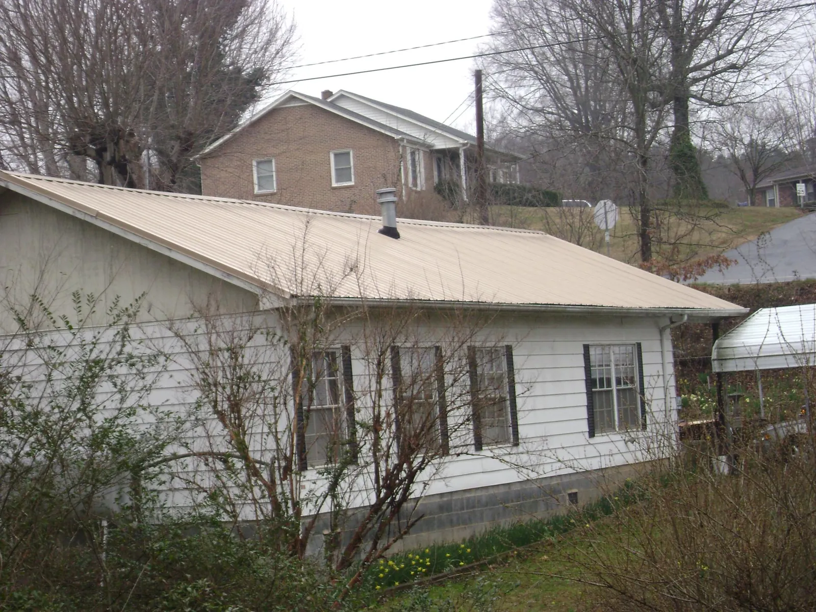 Tan metal roof on a white sided house set into a hillside — Commercial Roofing by Roofing Brothers in Ellisville