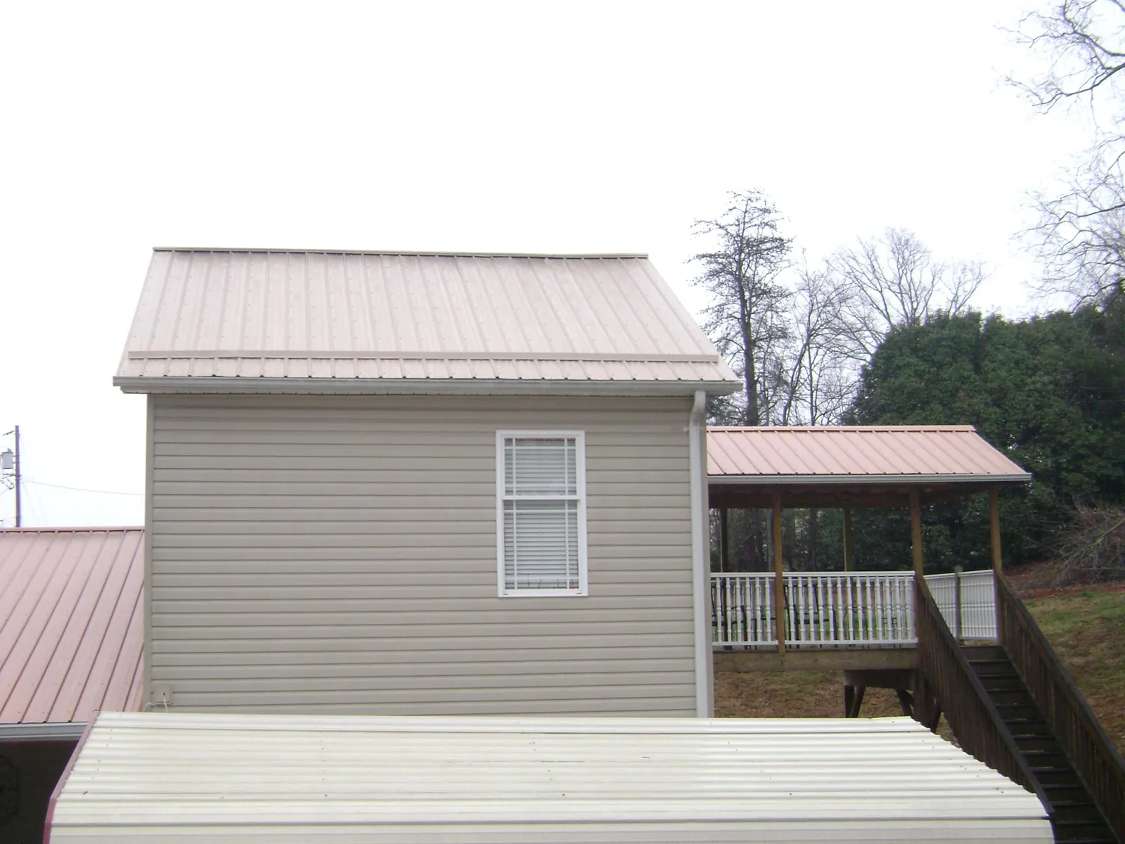 Tan metal roofs on a two story addition and attached porch, from a Roof Replacement job in Ellisville